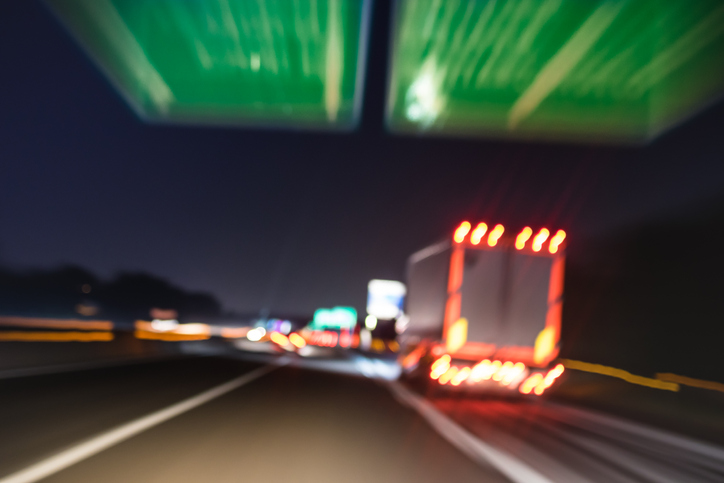  Defocused blurred motion of semi truck speeding on highway under street signs .
